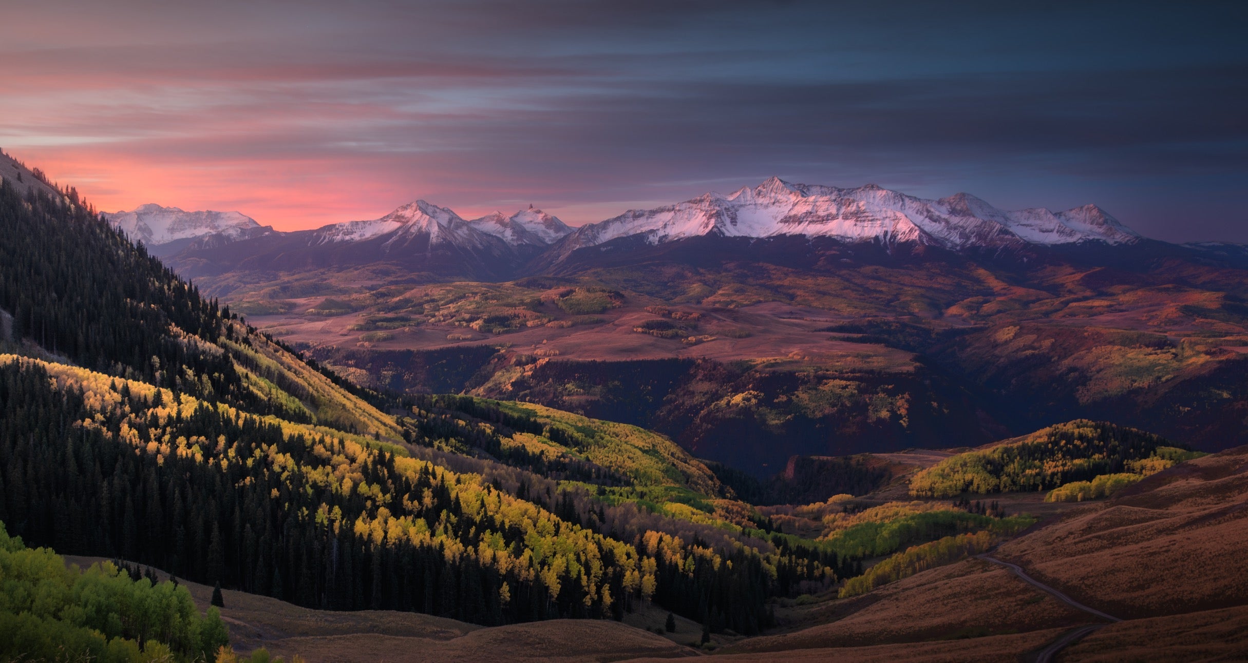 Mountain landscape with snow-capped peaks and a valley at sunset.